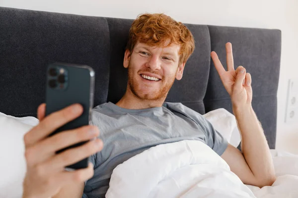 Gri Tişörtlü Gülümseyen Kızıl Saçlı Genç Adam Telefonuyla Selfie Çekiyor — Stok fotoğraf