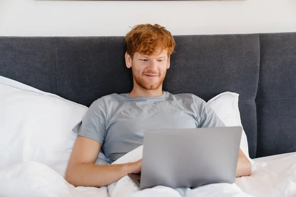 Mladý Pohledný Usměvavý Zrzka Muž Šedém Tričku Pracuje Notebookem Zatímco — Stock fotografie