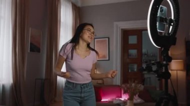 Yakışıklı Asyalı esmer kadın blogcu evde kameralı telefonda dans ediyor.
