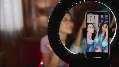 Şaşırmış çok ırklı kadın blogcular evde kameralı telefonda konuşuyor.