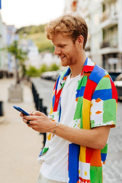 Mladý Pohledný Usmívající Zrzek Muž Strništěm Barevné Košili Drží Používá — Stock fotografie