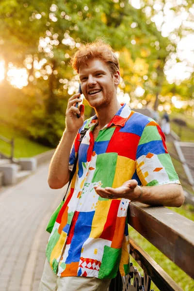 Mladý Pohledný Usměvavý Šťastný Muž Pestré Košili Mluvící Telefon Gestikuluje — Stock fotografie