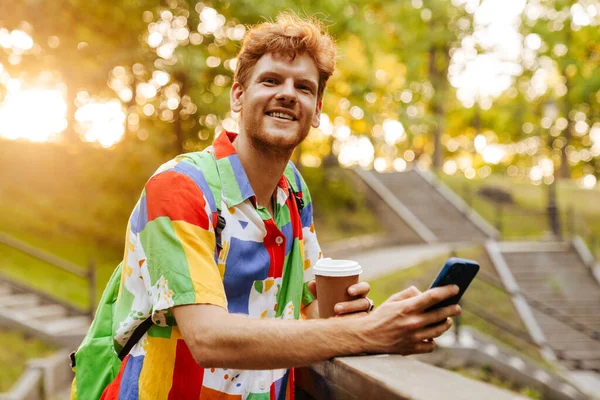 Mladý Pohledný Usměvavý Šťastný Muž Pestré Košili Kávou Telefonem Dívá — Stock fotografie