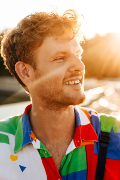 太陽の下で立っている間 脇を見てカラフルなシャツの若いハンサムな笑顔幸せな男の肖像画 — ストック写真