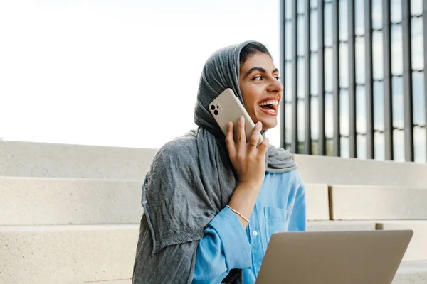 Jovem Mulher Muçulmana Usando Lenço Cabeça Usando Celular Laptop Enquanto — Fotografia de Stock