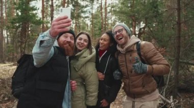 Çok uluslu gülümseyen turist arkadaşları ormanda telefonla selfie çekiyorlar.