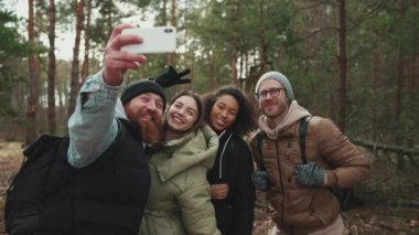 Mutlu çok uluslu turist arkadaşlar ormanda telefonla selfie çekiyorlar.