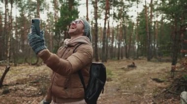 Şapkalı neşeli turist ormanda cep telefonuyla konuşuyor.