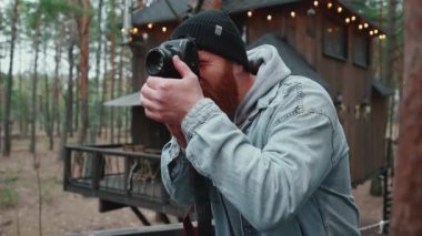 Yakışıklı kızıl saçlı adam ormanda kamerasıyla fotoğraf çekiyor.