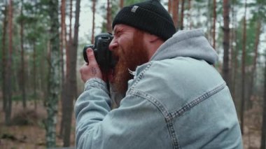 Neşeli kızıl saçlı adam ormanda fotoğraf çekiyor.