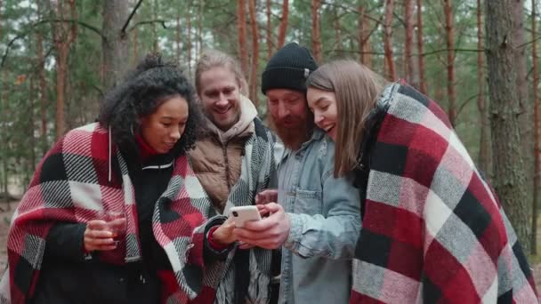 森の中の毛布で覆われたキャンプファイヤーの近くで携帯電話を話し 見て素敵な多国籍の友人 — ストック動画
