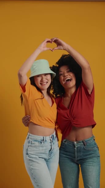 Smějící Nadnárodní Ženy Objímající Ukazující Gesto Tvaru Srdce Kameru Žlutém — Stock video
