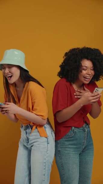 Zabawne Wielonarodowe Kobiety Smsujące Telefonach Stojąc Tyłem Żółtym Studio — Wideo stockowe