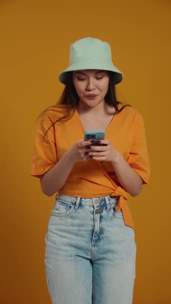Excited Asian Woman Wearing Panama Hat Texting Mobile Yellow Studio — Stock Video