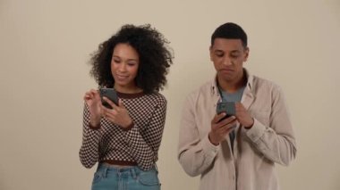 Pozitif Afrikalı genç çift bej rengi stüdyoda dururken telefonla mesajlaşıyor.