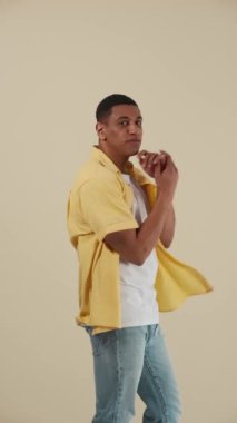 Bej stüdyoda kameraya poz veren gülen Afrikalı genç adam.