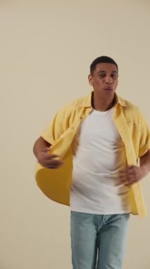 Yakışıklı Afrikalı genç adam bej rengi stüdyoda dans edip şarkı söylüyor.