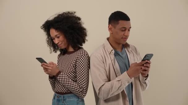 快乐的非洲年轻夫妇站在米色工作室里用电话打字 — 图库视频影像