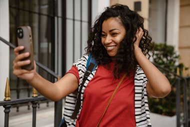 Genç siyahi kadın dışarıda beklerken cep telefonuyla selfie çekiyor.