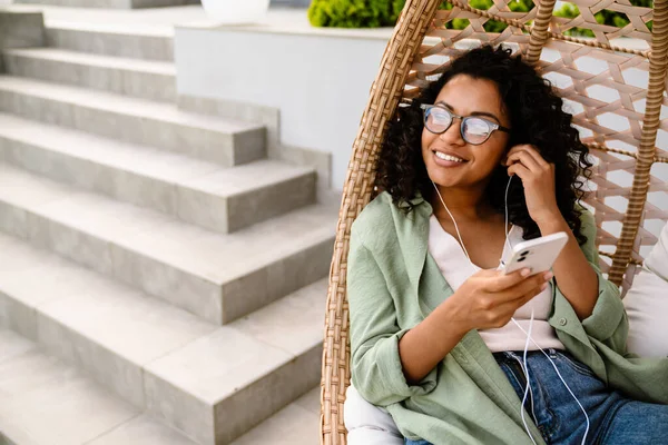 Cheerful Young African American Woman Eyeglasses Listening Music Earphones Smartphone — Stock Photo, Image