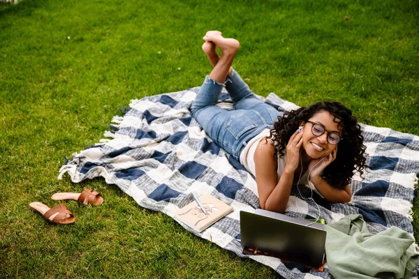 Young Cheerful Afro Woman Earphones Using Laptop While Lying Green — Stock Photo, Image