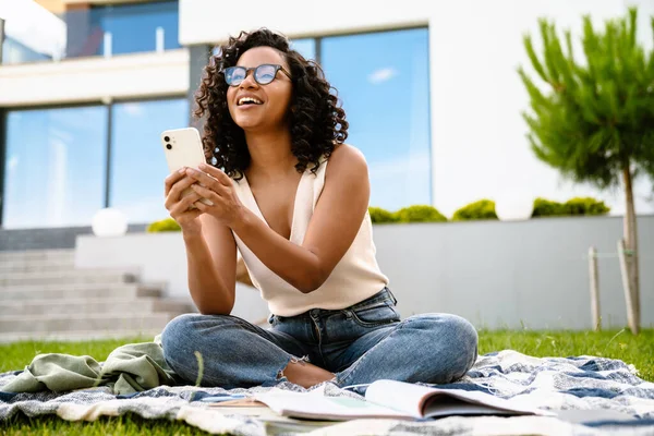 Glada Unga Afrikanska Kvinna Som Använder Mobiltelefon Medan Sitter Gräs — Stockfoto