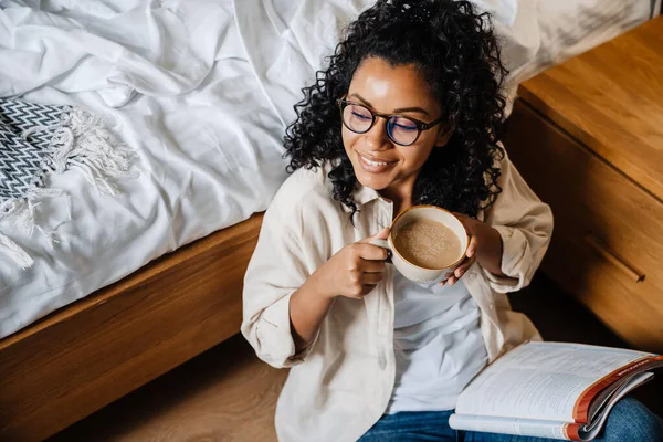 Afroamerykanka Młoda Kobieta Pije Kawę Podczas Nauki Zeszytem Ćwiczeń Sypialni — Zdjęcie stockowe