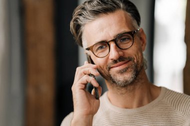 Gözlüklü, beyaz, orta yaşlı bir adamın cep telefonuyla konuştuğu yakın plan.