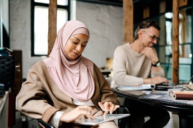 Bilgisayarlarla çalışan iki çok uluslu iş arkadaşı ofis masasında oturuyorlar.