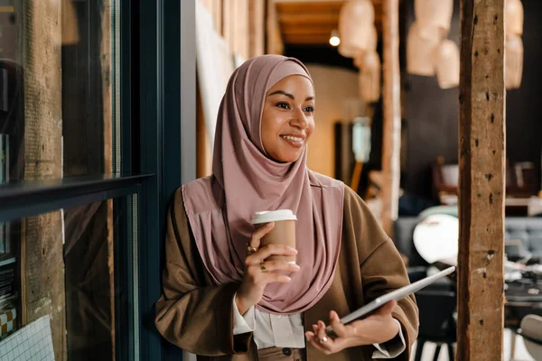 站在现代办公室时 快乐的阿拉伯女人头戴头巾 手里拿着咖啡和石碑 — 图库照片