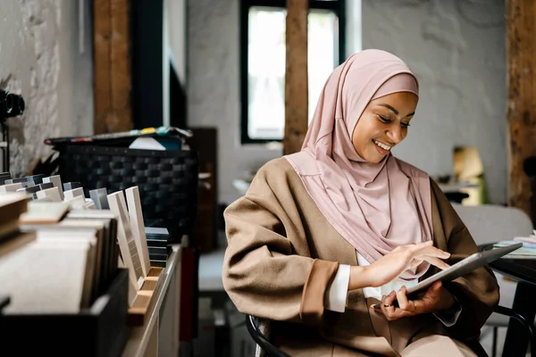 快乐的阿拉伯女性设计师穿着头巾在平板电脑上工作在车间 — 图库照片