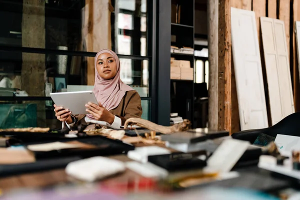 在车间穿着头巾在平板电脑上工作的多愁善感的阿拉伯女性设计师 — 图库照片