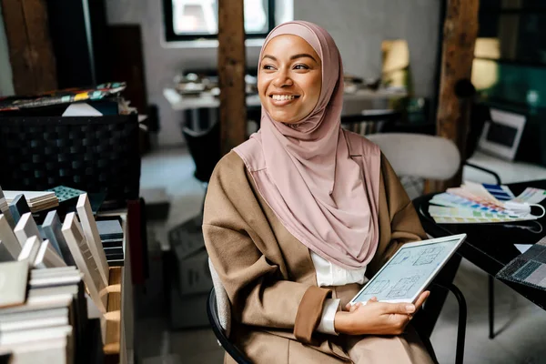 车间的女性快乐的穆斯林设计师穿着头巾在平板电脑上工作 — 图库照片