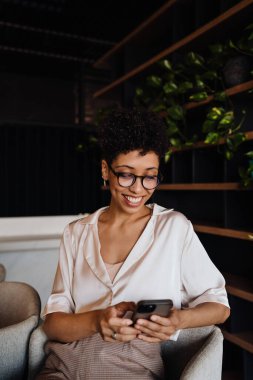 Orta yaşlı mutlu iş kadını kafede otururken cep telefonu kullanıyor.