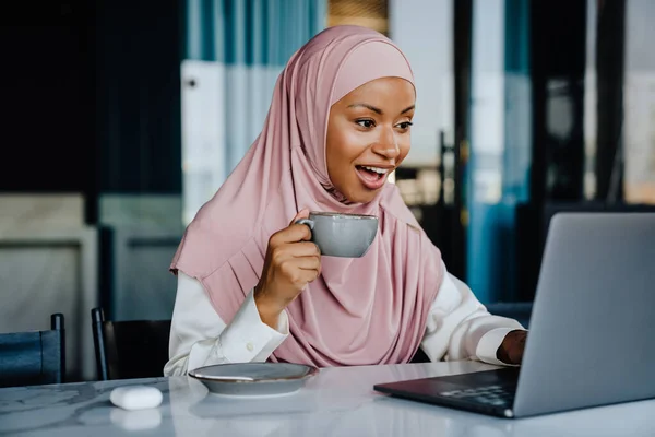 在办公室工作的穆斯林女商人一边喝咖啡一边用笔记本电脑 — 图库照片