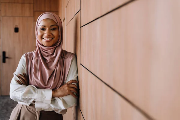 快乐的穆斯林女商人在办公室工作时微笑着站在墙边 — 图库照片