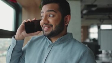 Ofisin penceresinin yanında telefonla konuşan mutlu Hintli adam.