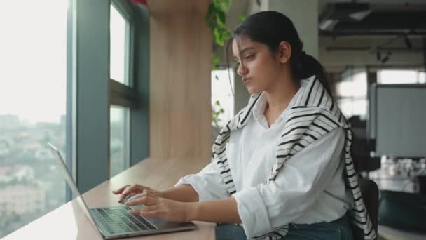 Συγκεντρωμένη Ινδή Γυναίκα Που Εργάζεται Φορητό Υπολογιστή Κοντά Στο Παράθυρο — Αρχείο Βίντεο