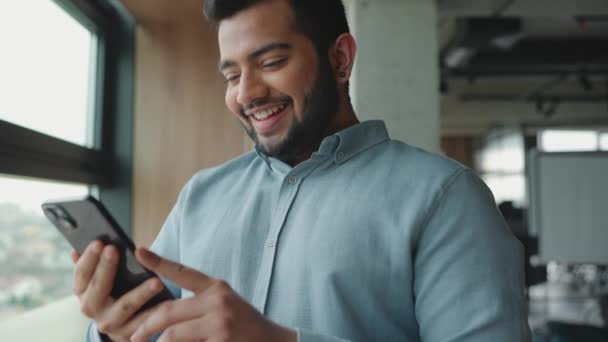 Nevető Indiai Férfi Sms Ezik Mobilon Miközben Ablak Mellett Irodában — Stock videók