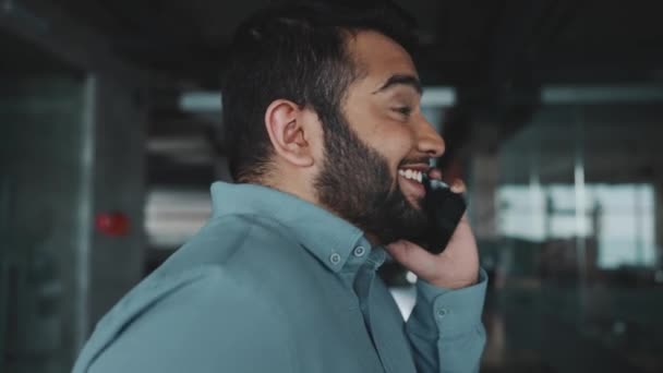 オフィスを歩いている間に電話で話しているインド人の男の笑顔 — ストック動画