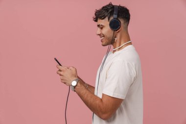 Young 'ın kulaklıklı, pembe izole edilmiş arka planda telefonu yanında duran şık bir gülümseyen adamı vardı.