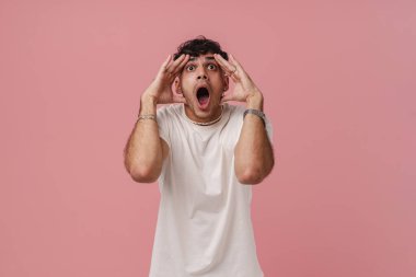 Geniş açık gözlü, ağzı ve gözleri ile genç ve yakışıklı bir adamın portresi iki eline dokunuyor ve yukarıya bakıyor, izole pembe arka planda dikilirken
