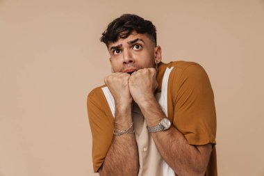 Esmer, korkmuş bir adam bej arka planda izole edilmiş kameraya el kol hareketi yapıyor.