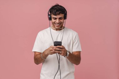 Pembe arka planda izole edilmiş cep telefonu kullanırken gülümseyen esmer bir genç adam.