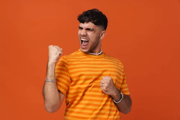 Brunette young man screaming while making winner gesture isolated over red background