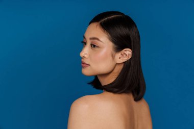 Çekici, çekici, sakin Asyalı bir kadının portresi. Arkası soyutlanmış mavi arka planda dikilirken yana bakıyor.