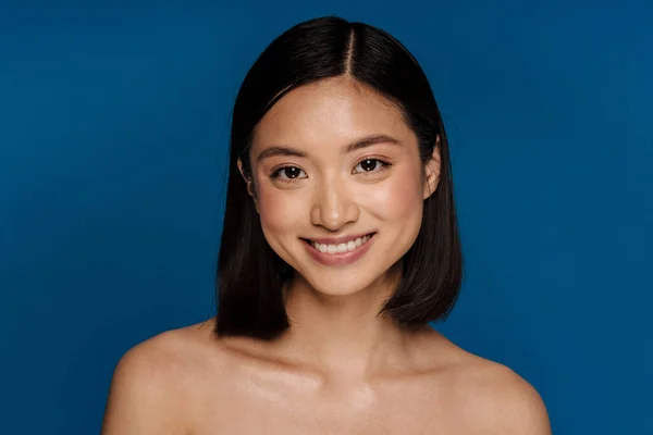Asian half-naked woman smiling and looking at camera isolated over blue background