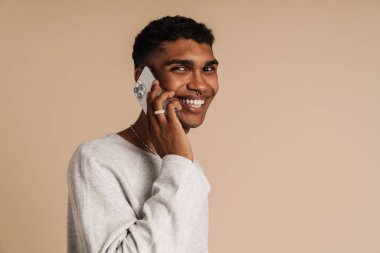 Genç yakışıklı, şık, gülümseyen Afrikalı adamın portresi. Telefondan konuşan ve kameraya bakan. Ayrı bej arka planda yan yana dururken.