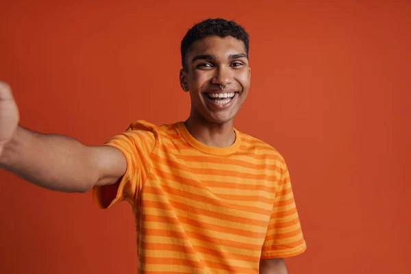 年轻英俊 笑容可亲 穿着T恤衫的非洲男子的自画像 一边看着相机 一边站在孤立的橙色背景上 — 图库照片
