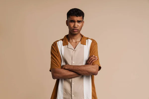 stock image Portrait of young handsome sad african man with piercing with folded arms looking at camera ,while standing over isolated beige background